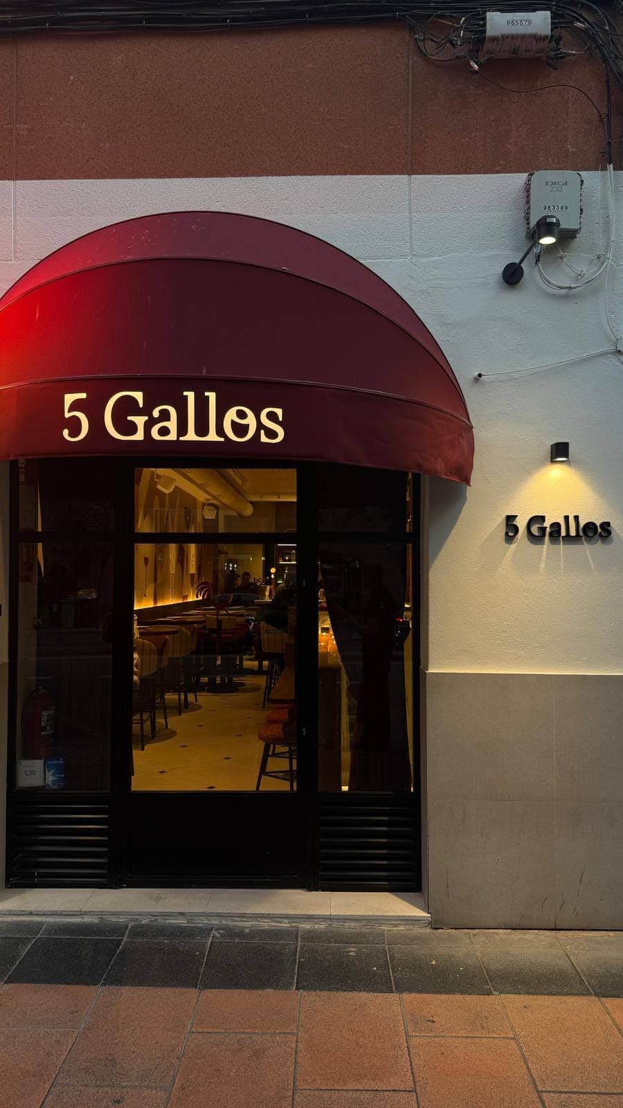 The 5 Gallos facade at dusk: wine-red awning with the name lit up and the sign on the wall