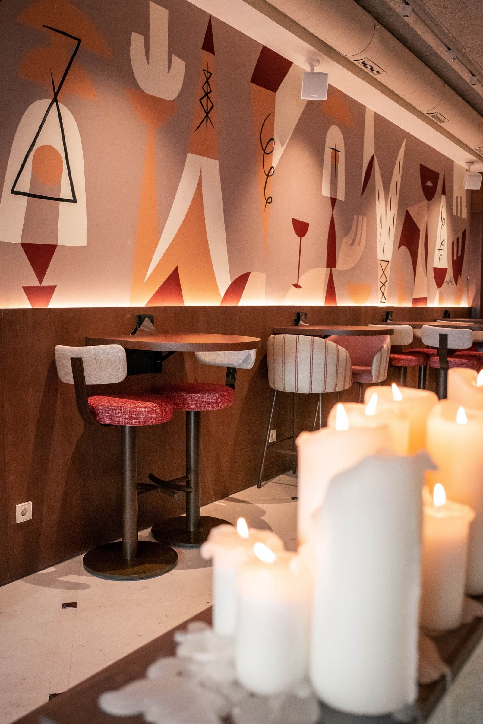 The 5 Gallos dining room: tall wooden tables and red stools beneath Teddy Kelly's mural, with candles in the foreground