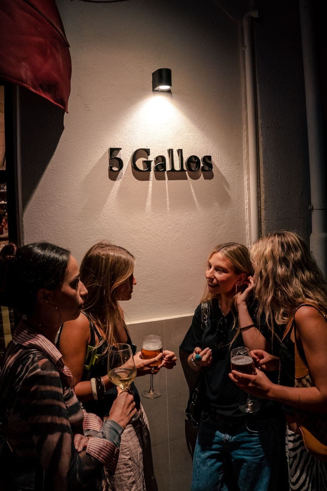 Four friends chatting over drinks beneath the 5 Gallos sign