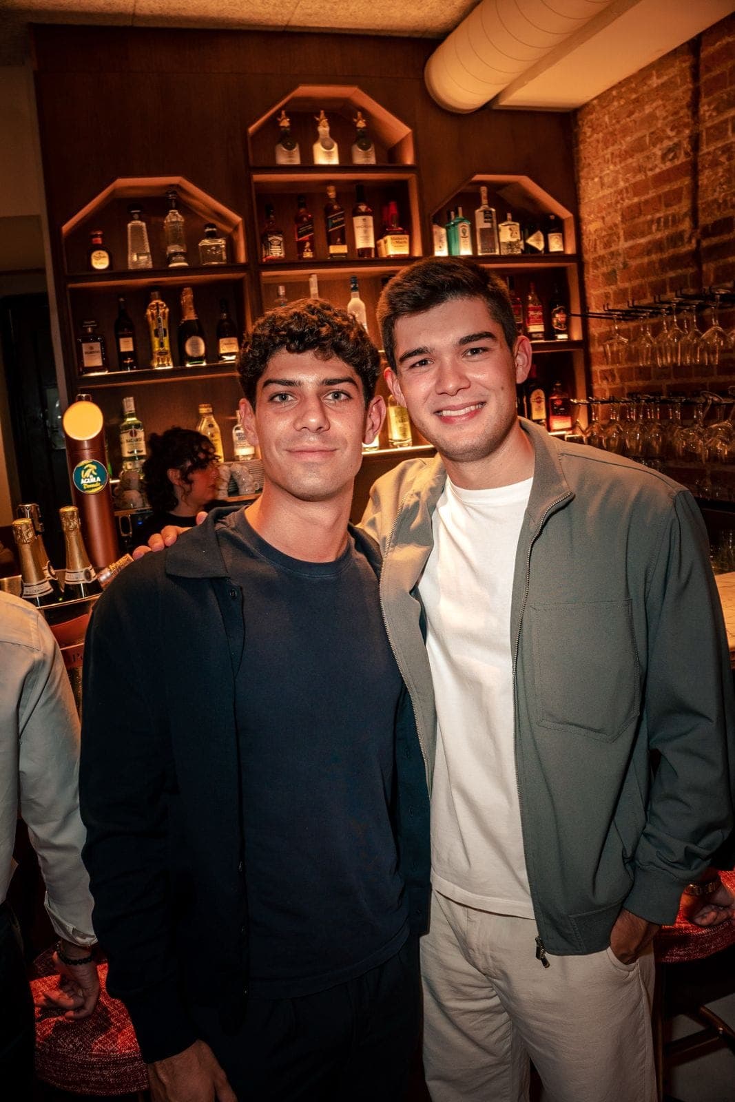 Two friends smiling in front of the back bar lined with bottles