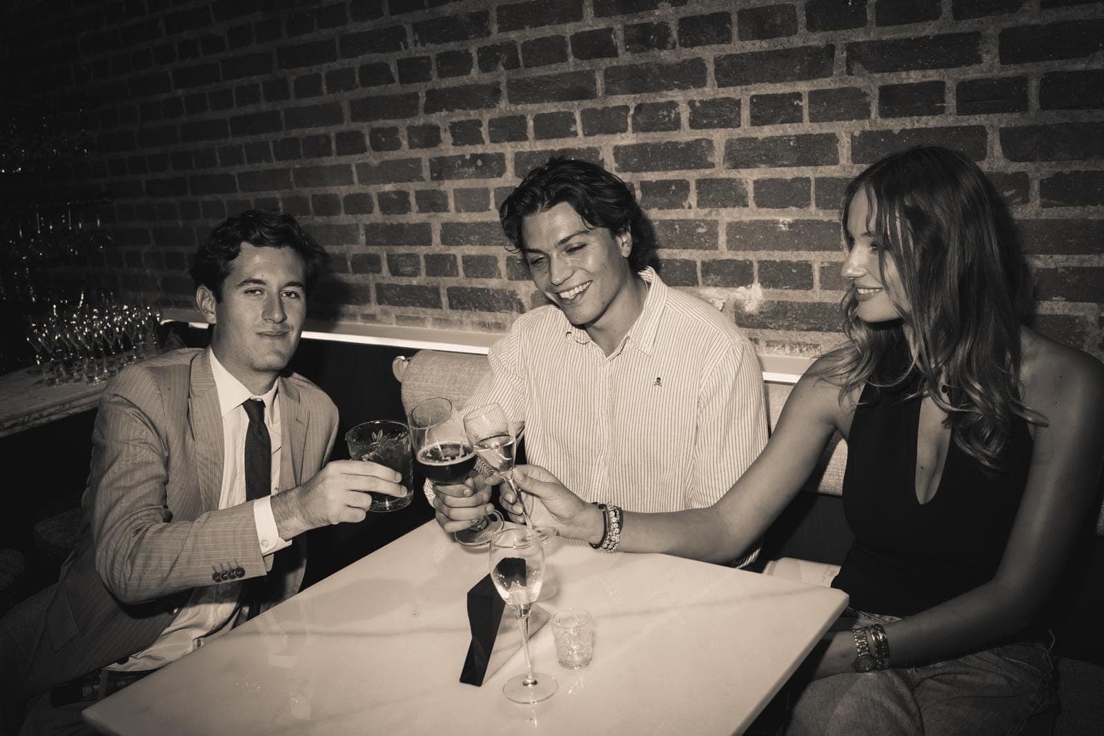 Three friends raising a toast on a sofa by the exposed brick wall