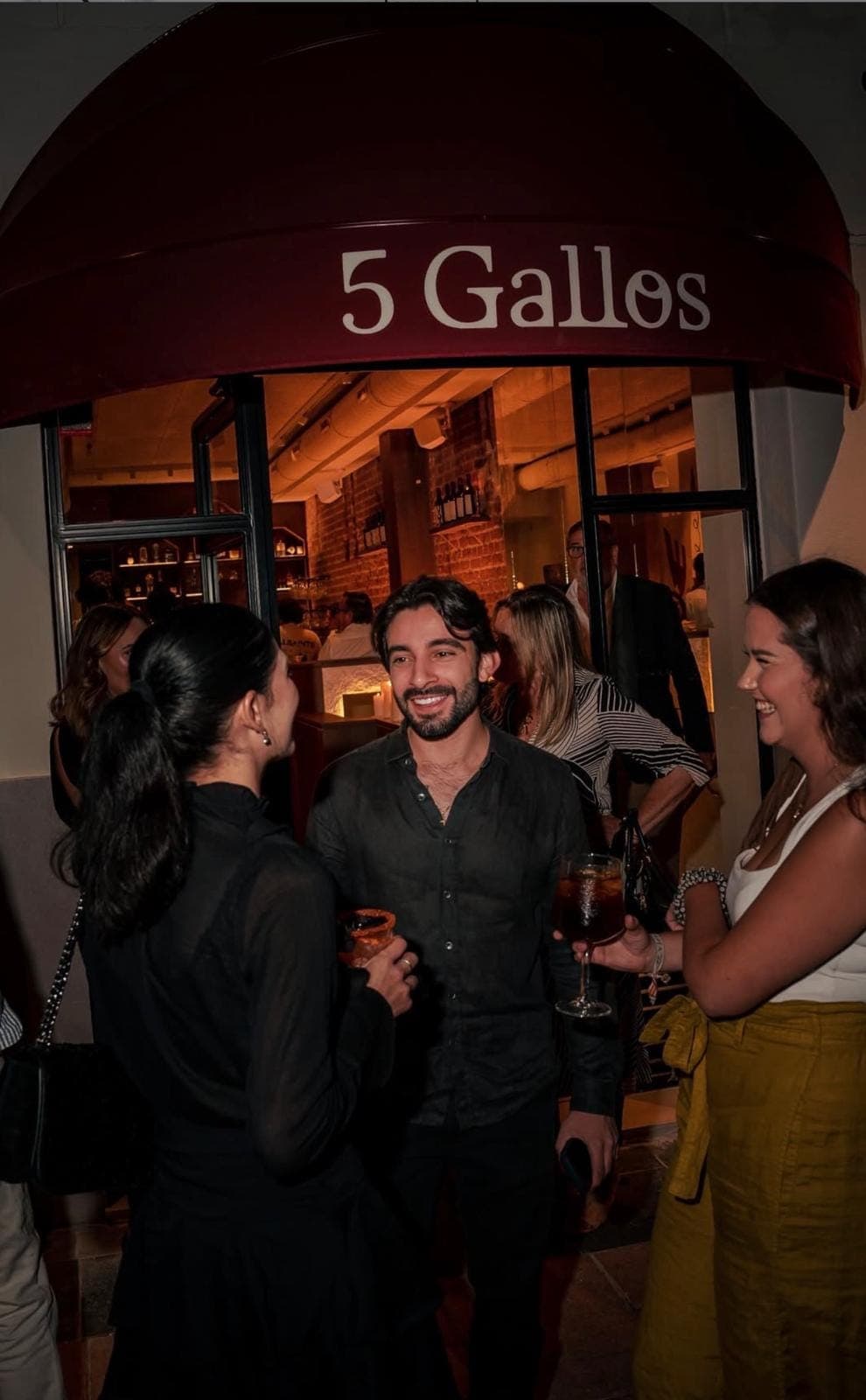 Charla con cóctel en mano en la puerta de 5 Gallos, bajo el toldo