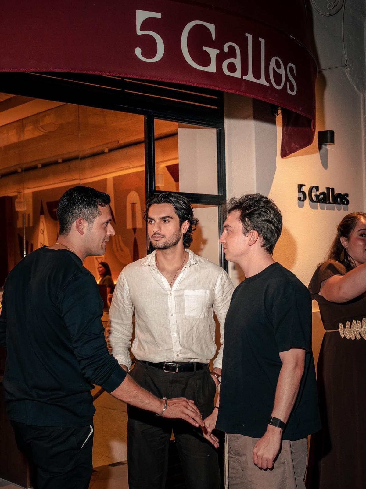 Three friends greeting each other at the entrance, under the wine-red awning