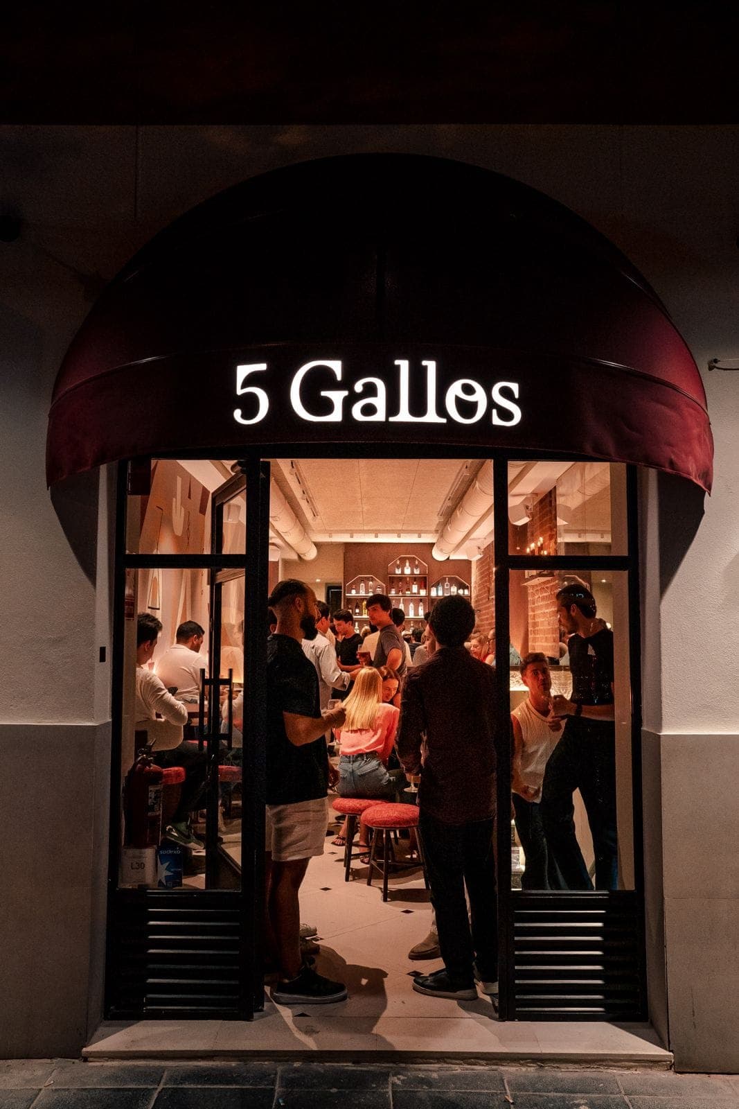The open door of 5 Gallos at night, with the awning lit up and a full dining room